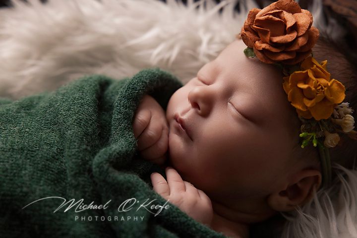 Artistic newborn portraits with baby on white fur and green fabric with orange flowers.