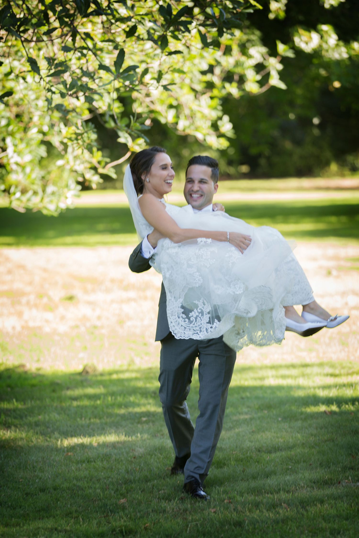 A groom carries his bride across a sunny garden lawn in a traditional wedding moment.