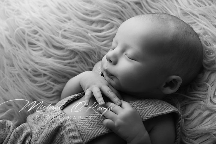 Black and white newborn photography of a sleeping baby resting on a fluffy rug, hands folded peacefully.