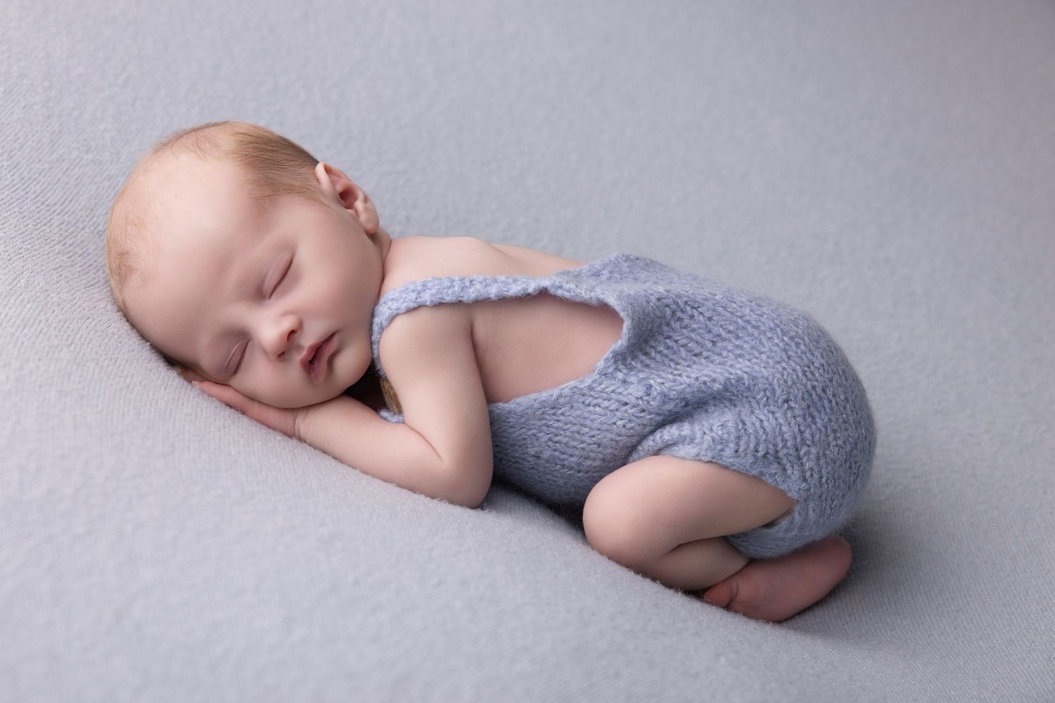 A sleeping baby in a grey knit wrap lies peacefully on a soft grey backdrop in a series of artistic portraits.