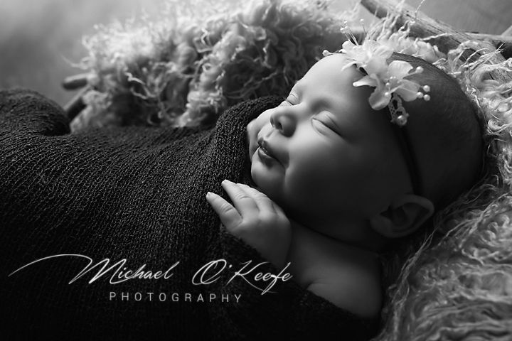 Black and white newborn photography of a sleeping baby with a flower headband by Michael O'Keefe Photography.