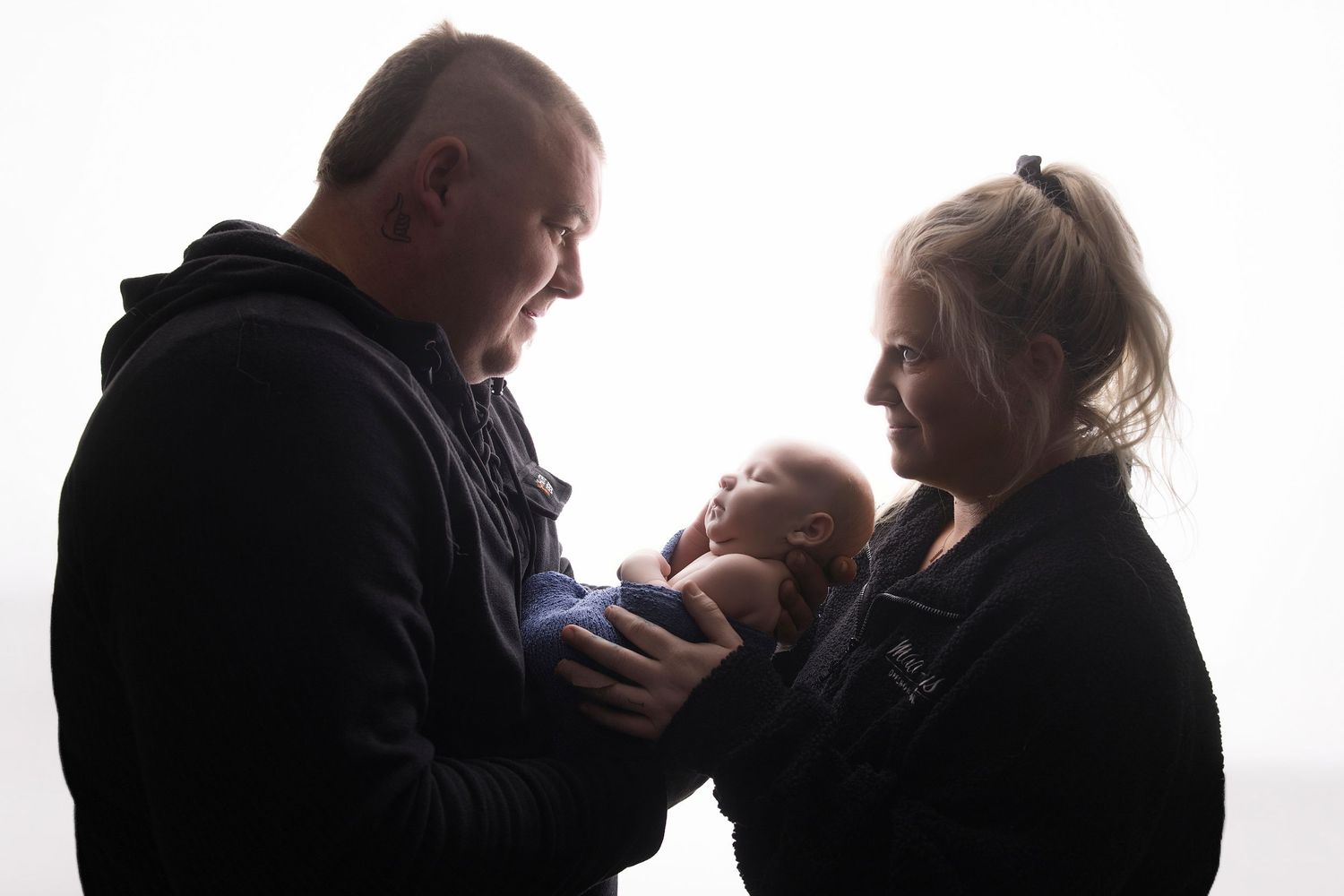 Parents lovingly holding their newborn baby in a tender family portrait with soft backlit lighting.
