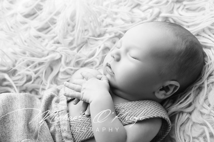 A sleeping infant rests peacefully on a white fluffy blanket in black and white photography.