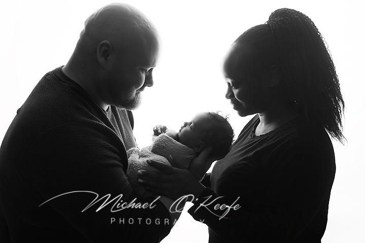 Black and white newborn photo of parents cradling their baby, captured by Michael O'Keefe Photography.