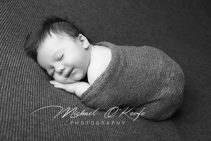 A series of black and white newborn photography portraits showing a sleeping baby in cozy poses on textured fabric.