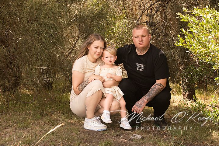 A family sits together outdoors for a portrait session against a natural backdrop of grass and foliage.