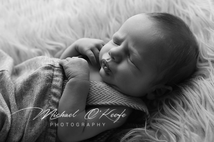 Black and white portrait of a sleeping newborn baby wrapped in a soft blanket on a furry backdrop.