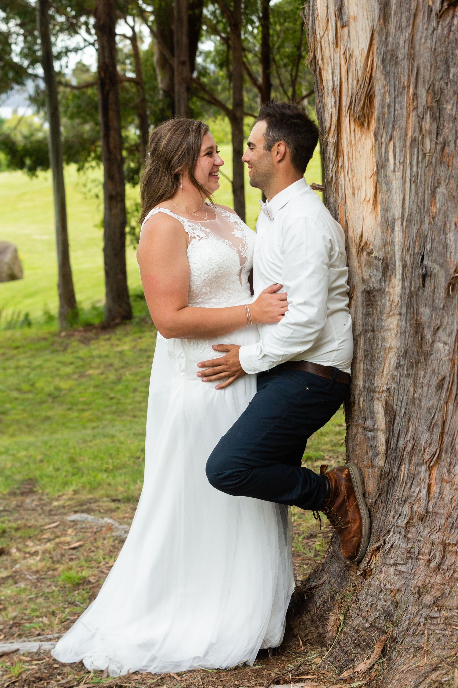Playful wedding photo sequence against large tree trunks in a wooded setting.