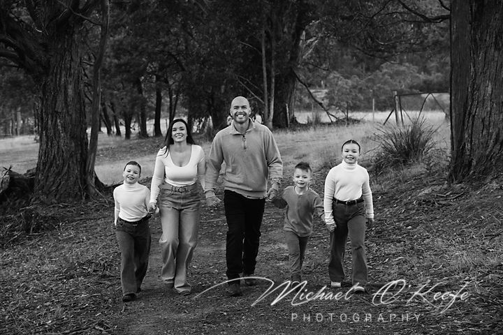 Wide angle family portrait in moody black and white against forest backdrop.