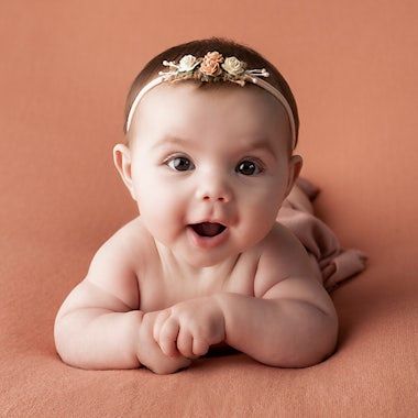 Sweet newborn photography with coral backdrop and delicate headpiece details.