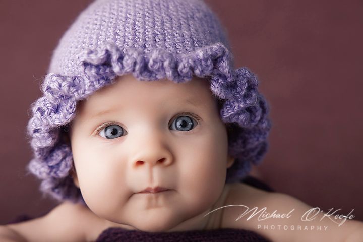 Adorable baby with blue eyes wearing a purple knit hat with ruffled brim, photographed by Michael O'Keefe Photography.