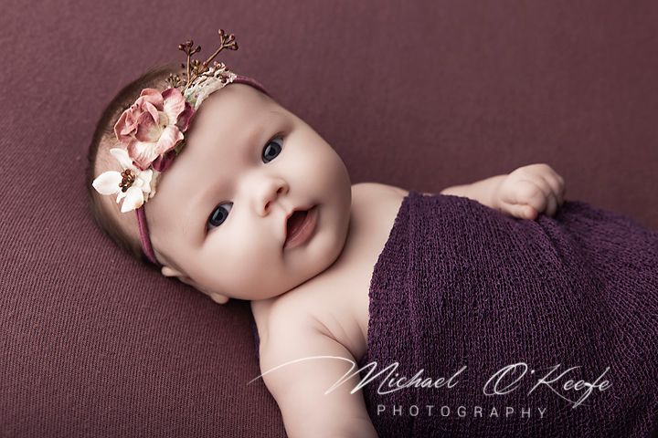 Newborn baby girl wearing purple wrap and floral crown headband, professional infant photography by Michael O'Keefe.