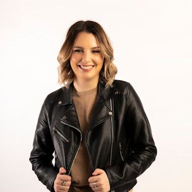 Person wearing black leather jacket poses in studio against white background.