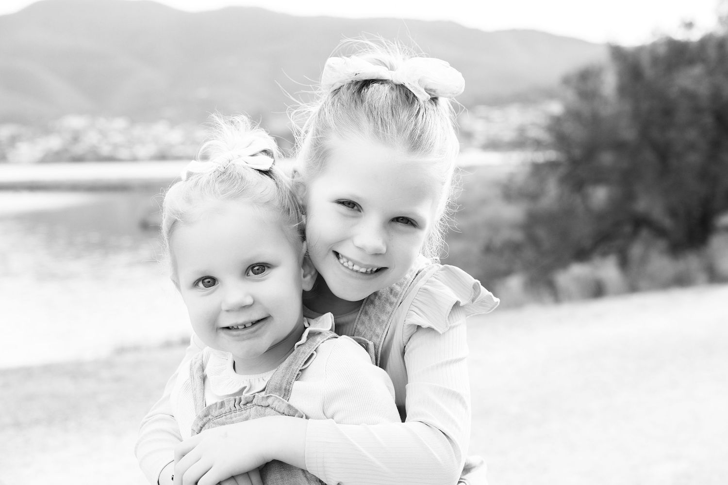 Black and white portrait showing outdoor affection between two young siblings by a lake.
