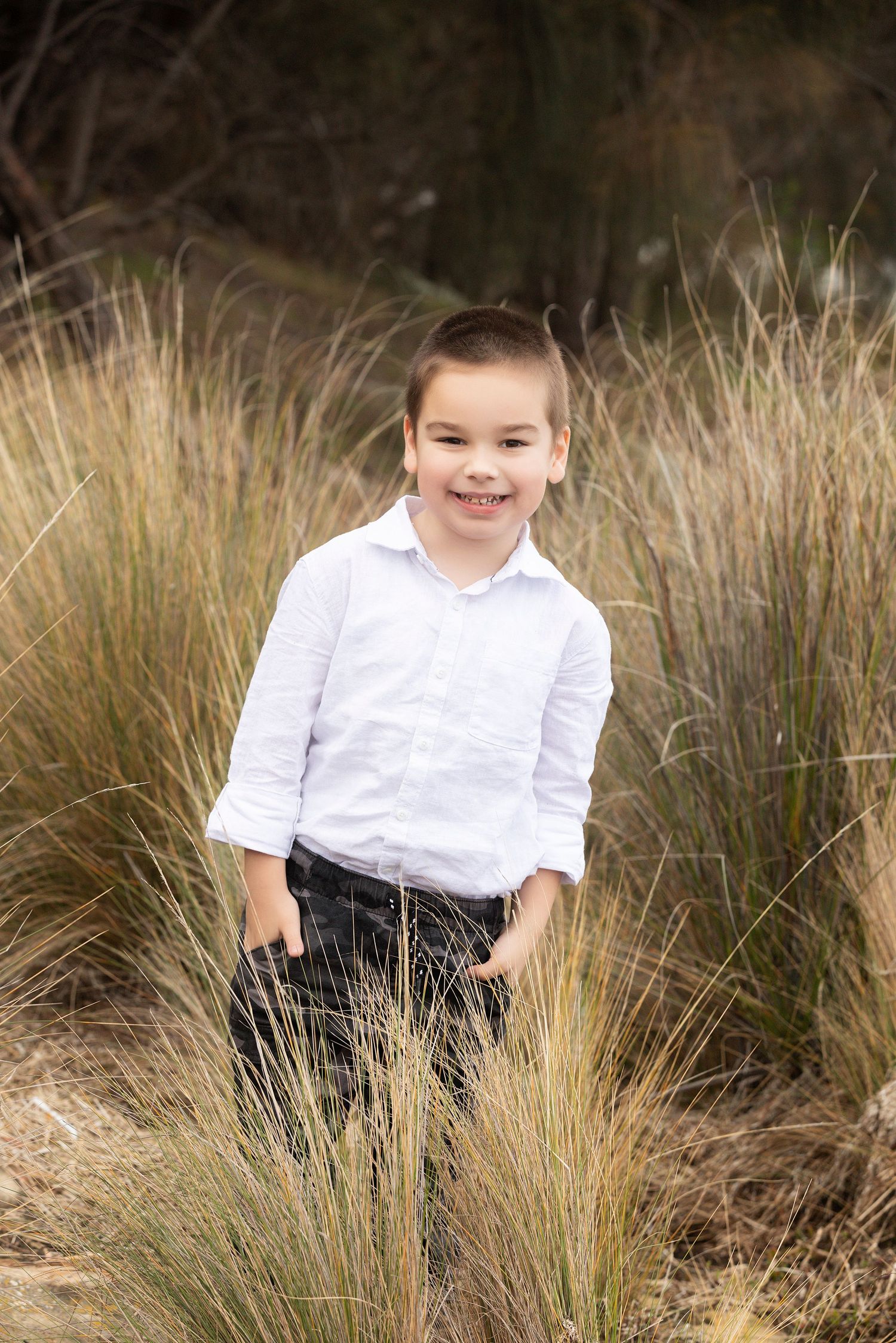 Child in white shirt sits among golden grass during outdoor portrait session.