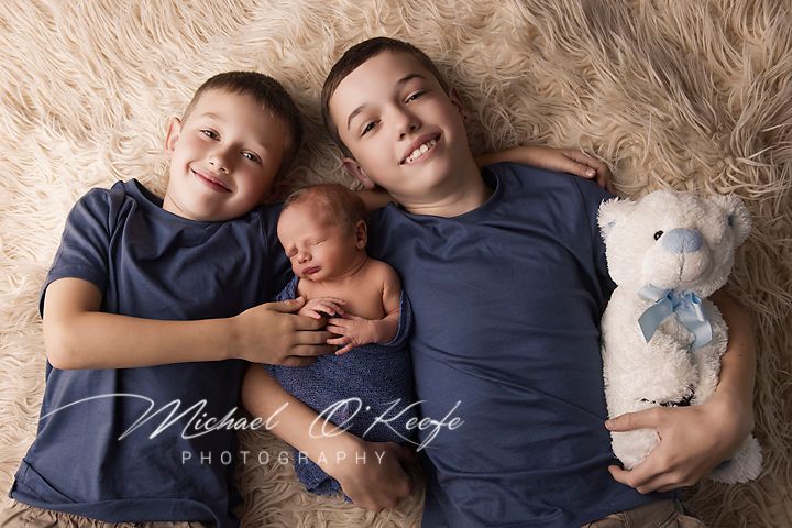 A cozy family photo session on soft beige carpet featuring matching navy blue outfits and a white teddy bear.
