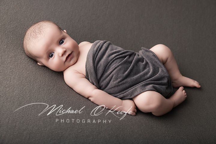 Newborn baby wrapped in gray cloth lying on gray backdrop, Michael O'Keefe Photography professional portrait.