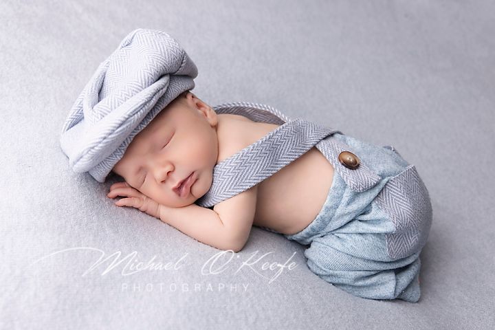 A sleeping newborn baby in gray and blue clothing rests peacefully in a series of five sequential poses.