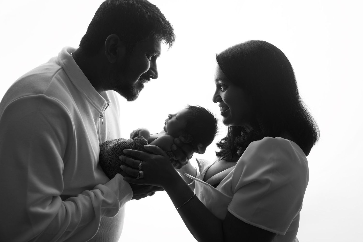 Black and white silhouette of new parents tenderly holding their newborn baby.