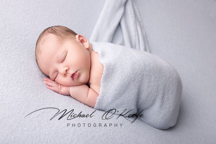 Sleeping newborn baby wrapped in soft gray swaddle blanket during professional photography session.