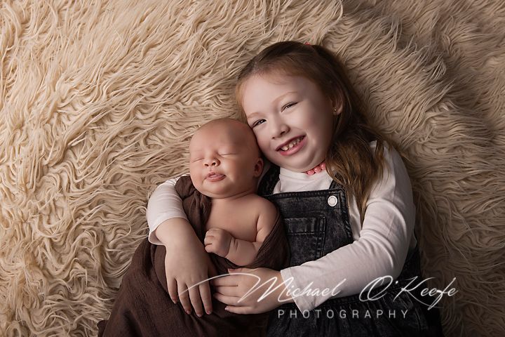 A newborn baby sleeps peacefully on soft beige textured fabric in a professional studio setting.