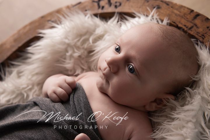 A baby lies on soft white fur for a newborn photo session in muted neutral tones.