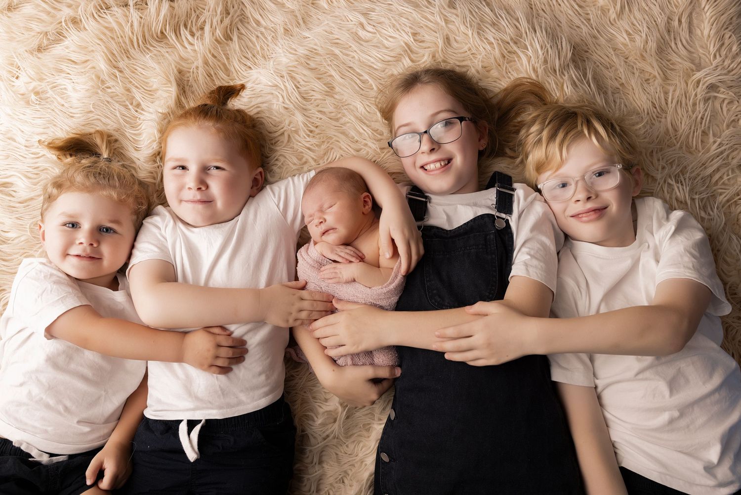 Family members lying in a row on cream colored backdrop wearing white clothing.