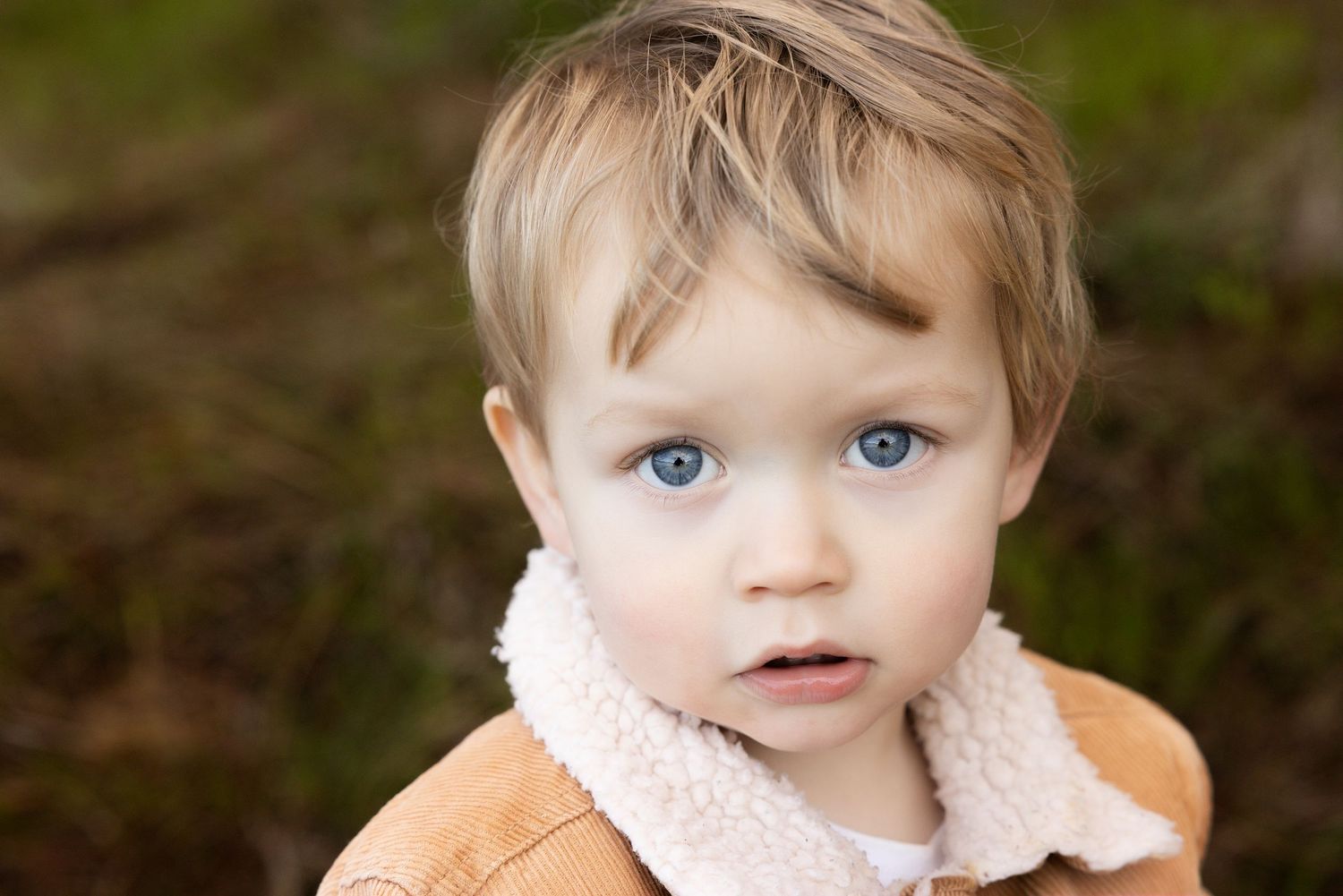 Close up portraits of a young child with light hair against natural backdrop.