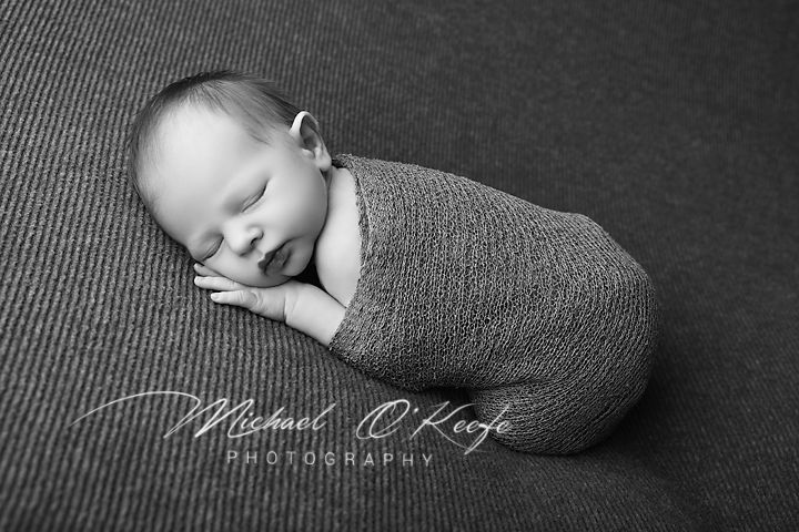 Black and white newborn photo of sleeping baby swaddled in knit wrap by Michael O'Keefe Photography.
