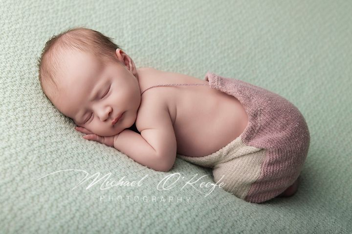 Sleeping newborn baby in pink knit shorts posed on mint green blanket in professional newborn photography session.