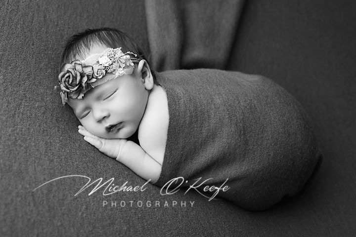 Black and white newborn photography with baby wrapped in gray swaddle wearing delicate floral headband.