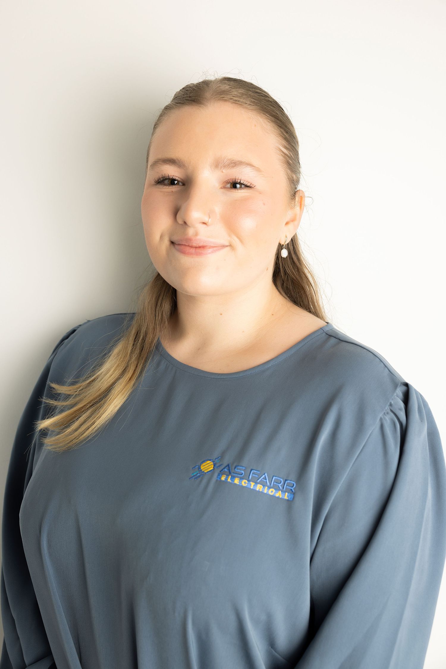 A close-up portrait of a person in a blue company shirt against a light background.