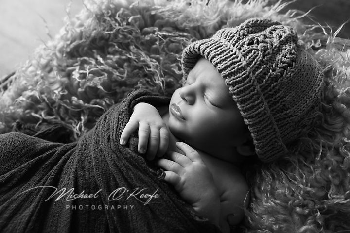 Sleeping newborn wearing knit beanie on textured brown backdrop.