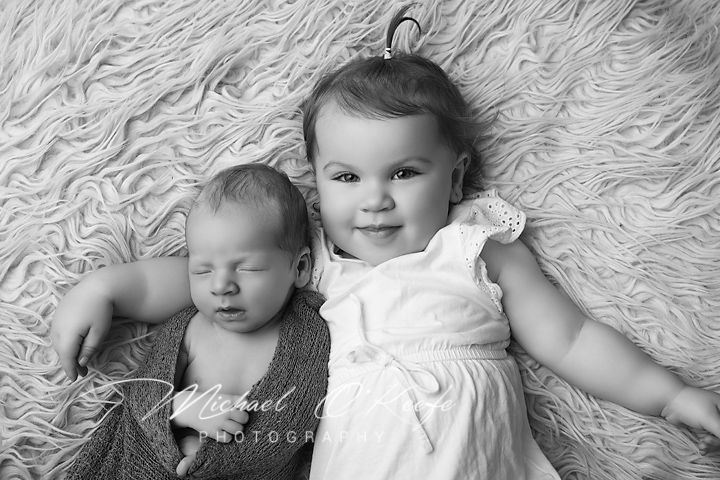 Two young children lying on a textured white blanket in black and white portrait photography.