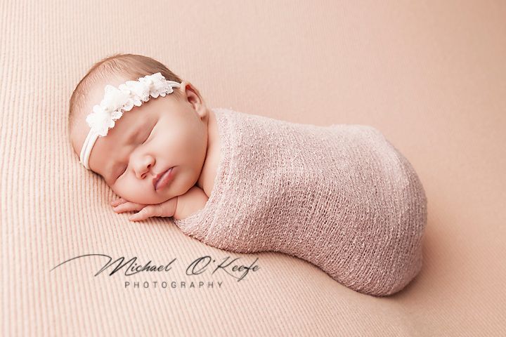 Newborn baby wrapped in soft pink blanket sleeping peacefully on textured background.