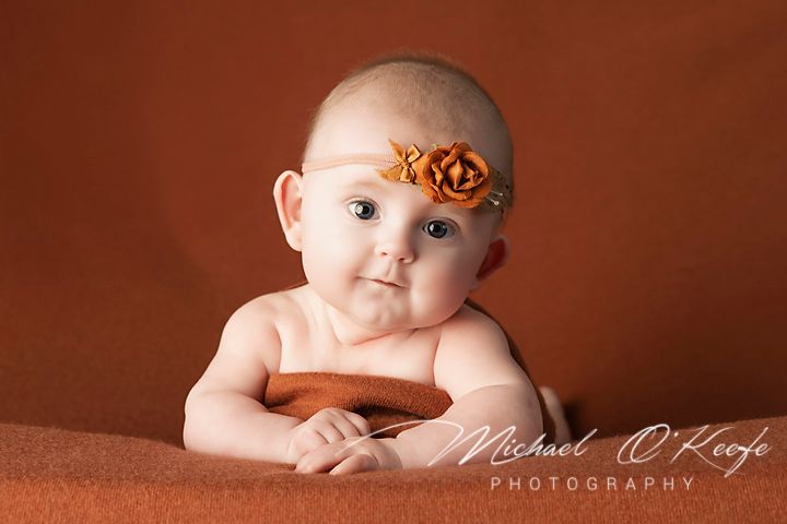 A baby lies on a brown backdrop during a professional studio photo session.