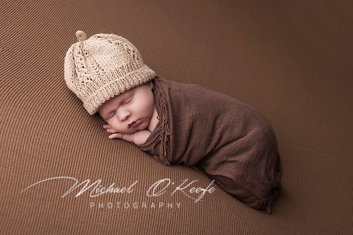 Professional studio portrait of sleeping newborn in cozy brown environment.