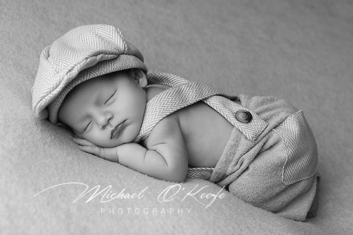 Serene black and white portrait of sleeping baby in vintage cap and overalls.