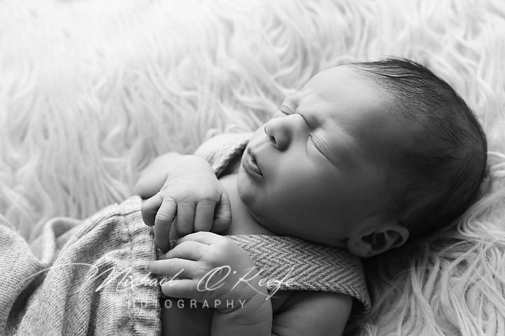 A sleeping infant lies peacefully on soft fluffy white fur with delicate lighting creating a dreamy atmosphere.