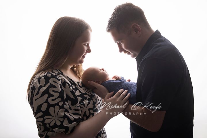 New parents tenderly cradle their newborn baby in a bright studio portrait by Michael OKeefe Photography.