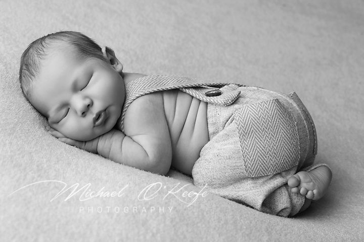 Peaceful newborn in soft lighting sleeping on side wearing knit shorts.