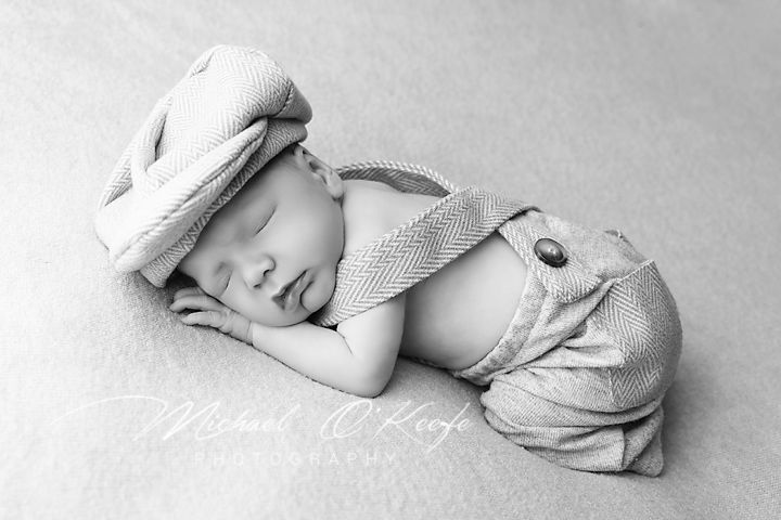 A black and white sleeping newborn baby lies curled up in soft white blankets in a serene sleeping position.