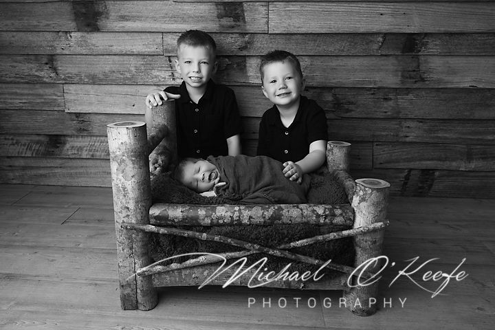 Black and white portrait series showing two children posing together on rustic wooden bench against wood plank wall.