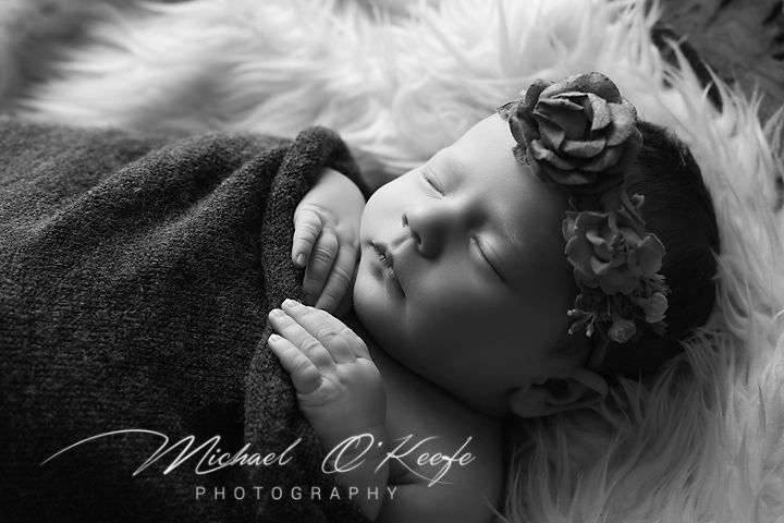 A black and white artistic portrait photograph of someone reclining on white fabric with dramatic lighting and shadows.