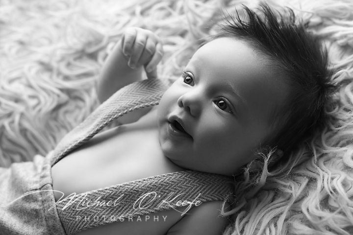 Black and white portrait of an infant lying on textured white fabric looking up with wide eyes.