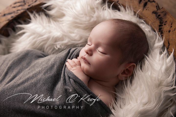 A newborn baby sleeps peacefully on soft white fur during a professional photography session.