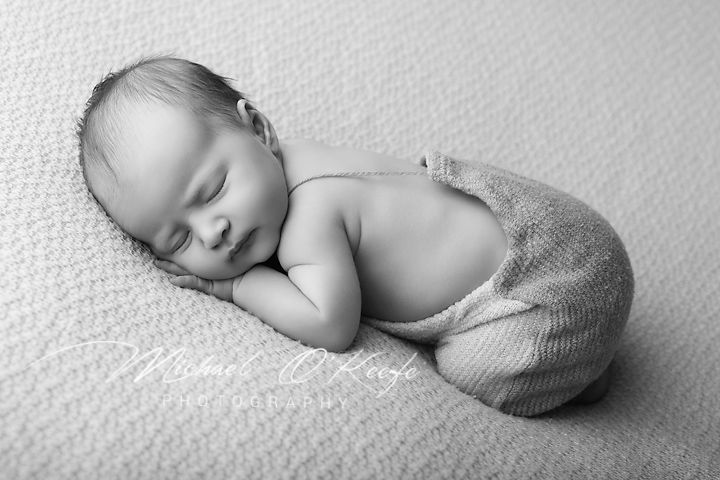 Black and white newborn photo of a sleeping baby curled up peacefully on a soft blanket.