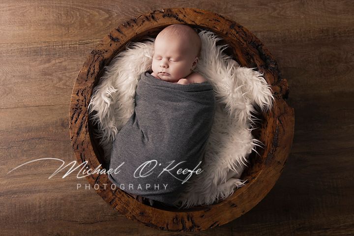 Artistic newborn photography with baby resting in wooden bowl against rustic backdrop.