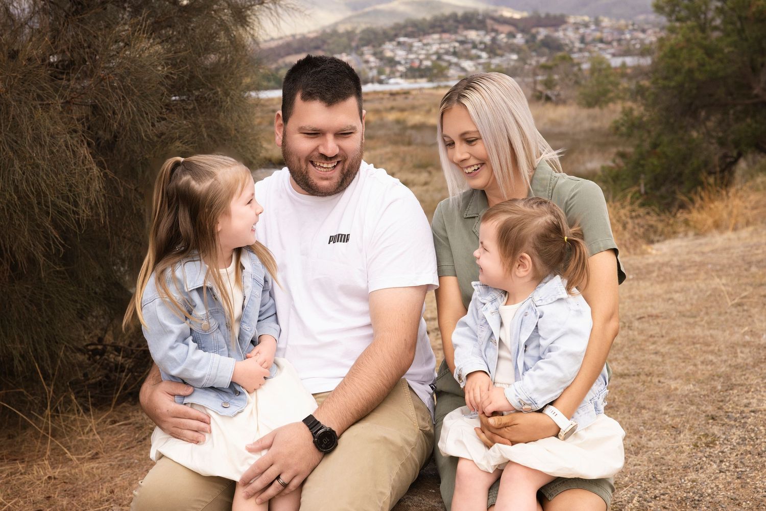 Family of four in casual wear sitting together outdoors on hillside.