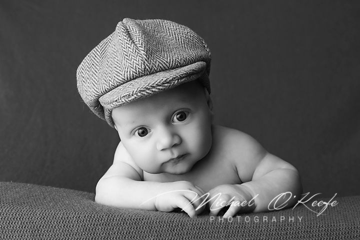 Black and white infant portrait featuring a newsboy cap across multiple artistic compositions against a dark background.